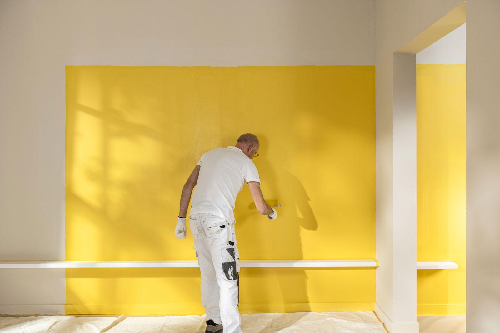 Photograph of a decorator painting a wall with yellow paint